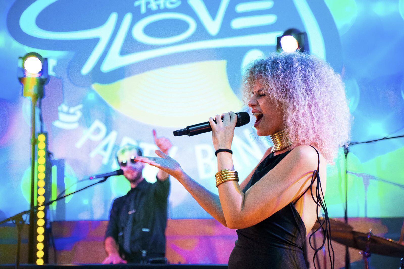 Female wedding singer performing under colorful lights with The Gloves logo projected behind her