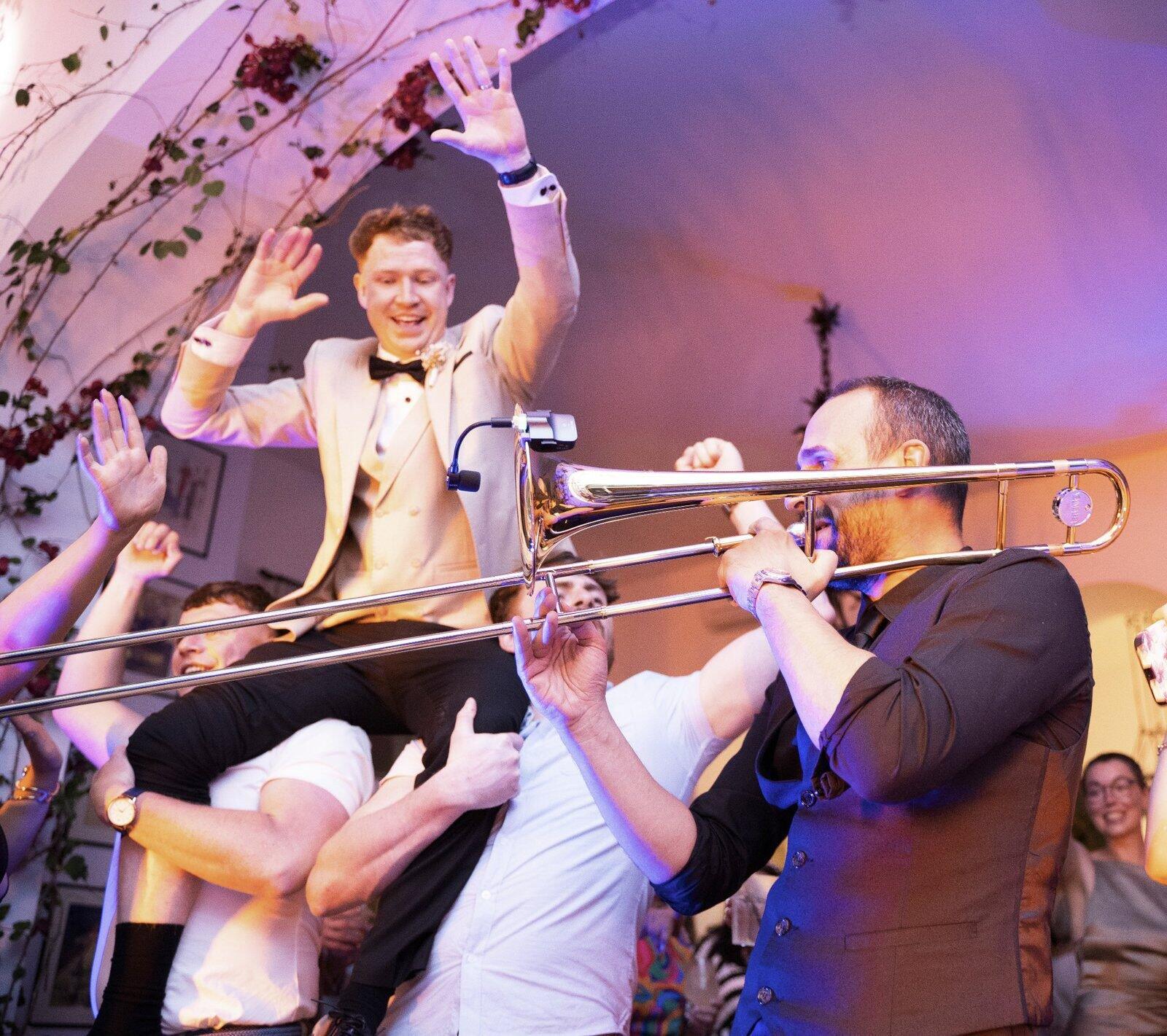 Groom lifted by friends while the wedding band plays trombone in a lively Italian wedding party
